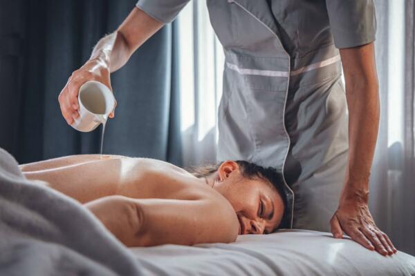 Eine entspannende Massage in einem Spa, mit einer Therapeutin, die Öl auf den Rücken eines Kunden gießt. Das sanfte Licht schafft eine ruhige und friedliche Atmosphäre.